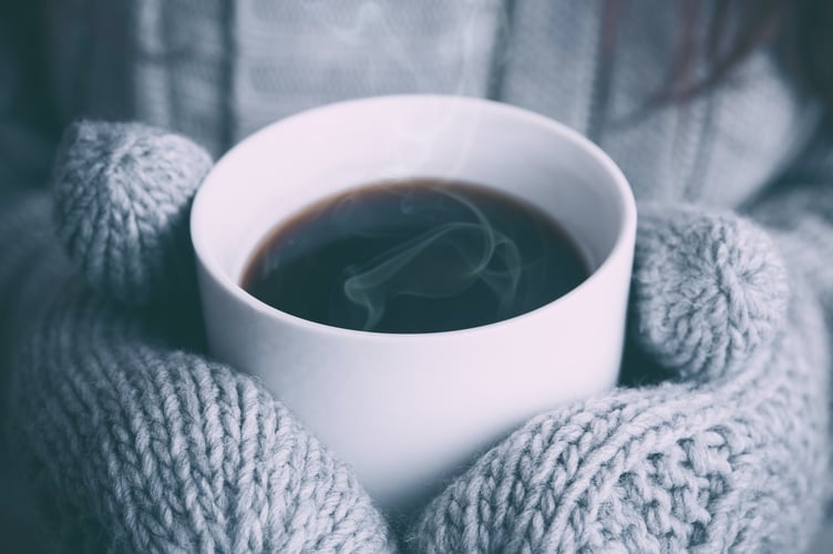 Gloved hands holding a cup of hot coffee