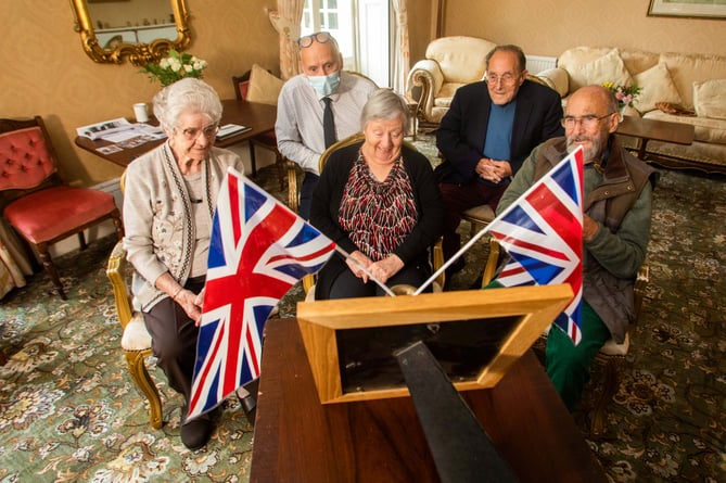 Residents at the Court House care home in Cheddar, Somerset, watch the Queen's funeral with owner Chris Dando,  on a television, with an iPad stuck to the screen, that was bought for the Queen's coronation. 19th September 2022. See SWNS story SWLNtelly. Care home residents gathered around a television bought for The Queen's coronation - to watch her funeral. The 25-strong group of pensioners - including one of the last to receive a card from Her Majesty for turning 100 just two weeks ago - huddled around the tiny set, just as many of them would have done nearly 70 years ago. They watched the service on the antique black and white Defiant set that was dusted off for the first time in decades. It was first used for an extended family to watch the Queen complete her formal accession to the throne in 1953.