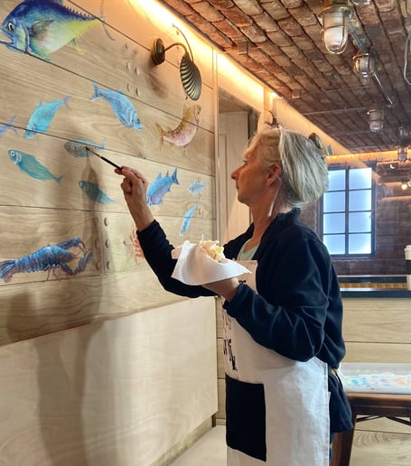 Sandy Bell painting the mural with a sandwich in hand