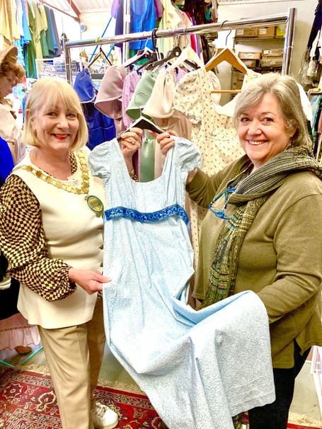  Rusette Auton (right) presents a Regency dress to Cllr Karen Walker, Chair of B&NES Council, standing before a collection of gowns created by Bath Theatrical, specifically for the Jane Austen 250th anniversary celebrations.