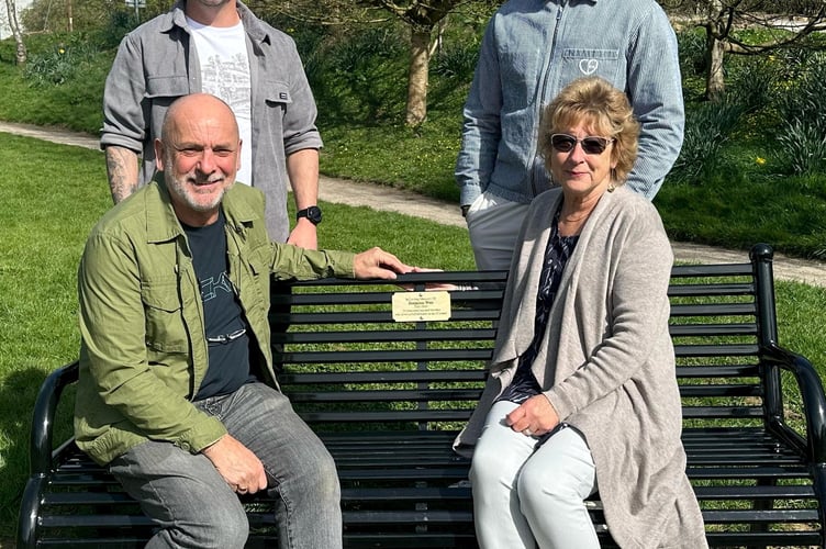 Jack and George with parents Robert Weir and Jane at the memorial bench for their  borther/son Benjamin at Ninesprings Country Park in Yeovil, Somerset. Photo released April 2 2025. Two brothers surprised their parents with a memorial bench in honor of their late sibling on Mother's day.Jack Weir, 40, and his younger brother George, 38, arranged for the bench to be installed at Ninesprings Country Park in Yeovil, Somerset, in honor of their older brother Benjamin, who passed away in 1999 at the age of 18.Their parents, Robert Weir, 69 and Jane, 68 had tried multiple times over the last two decades to get a bench where Benjamins ashes were buried but were repeatedly turned down by the council.Determined to make it happen, the brothers took matters into their own hands - secretly arranging for the bench to be installed and unveiling it as a surprise on Mothers Day.
